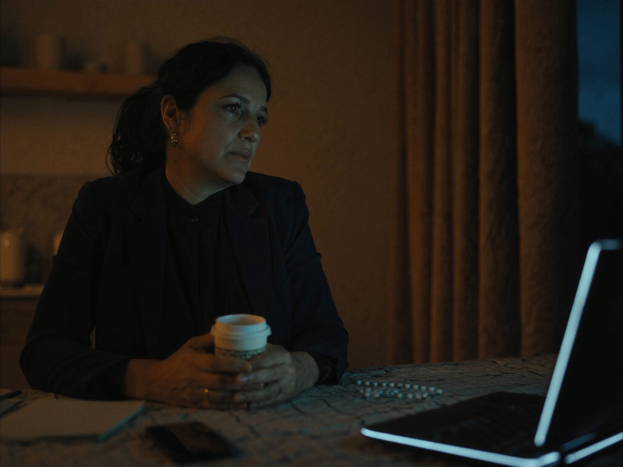 A working adult holding coffee while looking depleted at a laptop